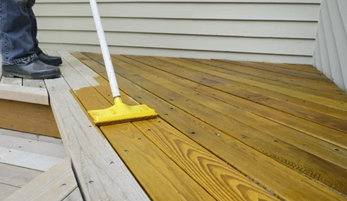 Applying wood stain to a deck surface with a roller to protect and enhance the wood.